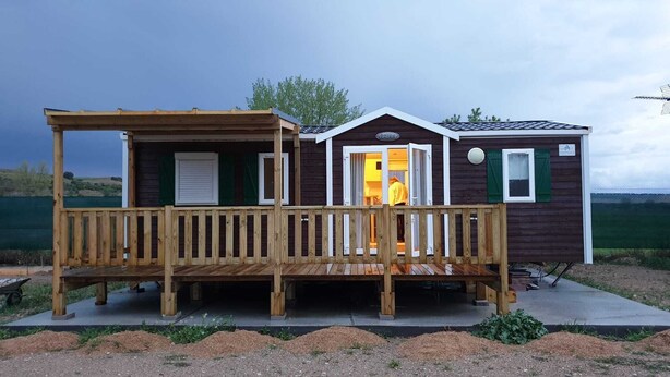 A small wooden cabin with a porch and a door leading to a room. - Independent cabins Las Rosas (Pollos Valladolid)