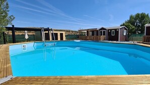 A clear blue swimming pool surrounded by wooden deck and wooden cabins. - Independent cabins Las Rosas (Pollos Valladolid)