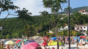 A beach with people sunbathing and swimming, a red running track, and a street lamp. - Studio apartment in Jadranovo with Balcony, Air condition, WIFI (3856-3) (Jadranovo)