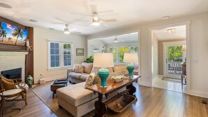 A spacious living room with hardwood floors, a fireplace, a sofa, a coffee table, and a ceiling fan. - Historic MamaDear House, Boca Grande Island w/private pool, 5min stroll to beach (Boca Grande)