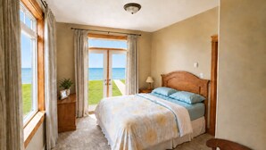 Une chambre à coucher avec un lit, des rideaux, une table de chevet, une lampe, une vue sur la mer et un luminaire au plafond.