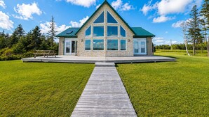 Une maison moderne dotée d’un grand porche à l’avant, d’un toit triangulaire et d’une terrasse en bois menant à l’entrée.