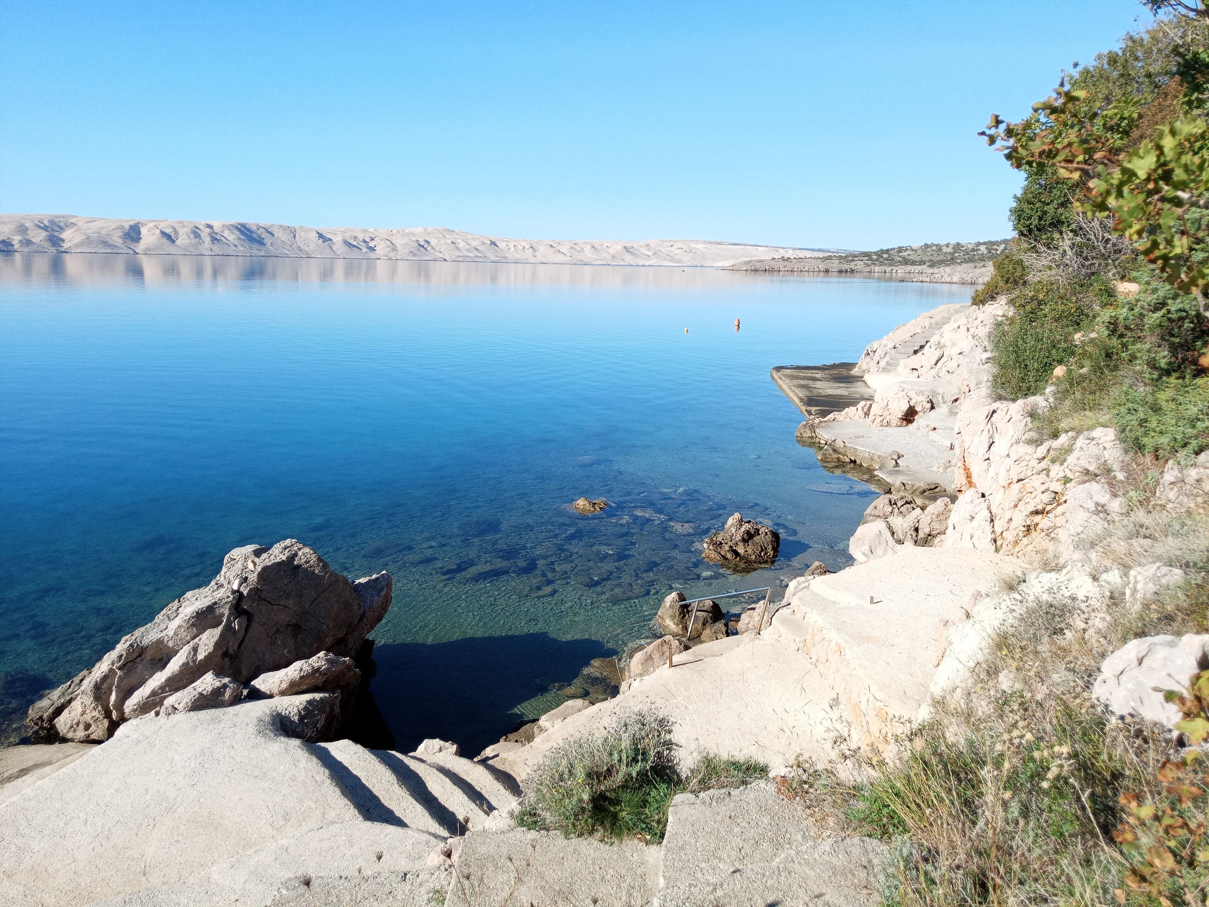 Paesaggio costiero con acque cristalline blu, scogliere rocciose e vegetazione rada.