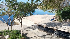 A beachside area with a concrete pathway, a metal bench, and a tree. - Wohnung Tonka für Einen Ruhigen Urlaub am Meer und Bergen (Karlobag, Cesarica, Ribarica)