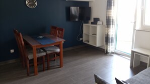 A dining area with a wooden table and chairs, a TV mounted on the wall, and a white shelving unit. - Wohnung Tonka für Einen Ruhigen Urlaub am Meer und Bergen (Karlobag, Cesarica, Ribarica)