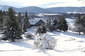 Paisaje nevado con una cabaña de madera, árboles cubiertos de nieve y una vista despejada de montañas distantes.