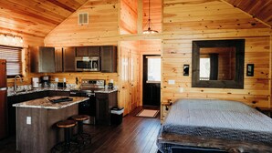 A log cabin interior with a kitchen, dining area, and a large bed. - Cozy cabin for up to 6 guests - Hocking Hills - Firepit -Hot Tub - Wifi (Logan)