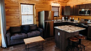 A compact kitchen with wooden walls, a built-in refrigerator, a microwave, and a small island with stools. - Cozy cabin for up to 6 guests - Hocking Hills - Firepit -Hot Tub - Wifi (Logan)
