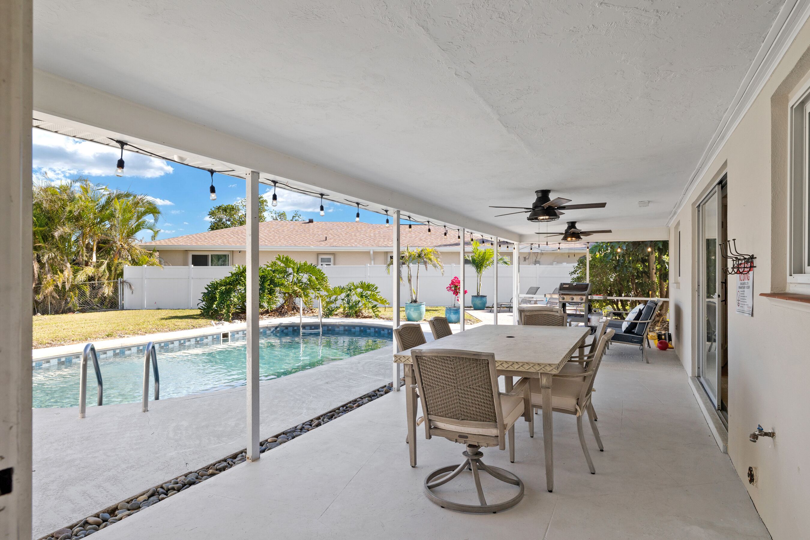A covered patio with a pool, outdoor furniture, and ceiling fans.