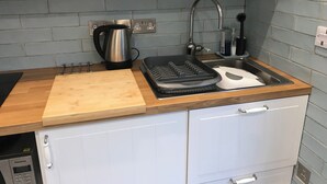 Une cuisine avec un plan de travail en bois, une bouilloire, un grille-pain et un évier avec un robinet.