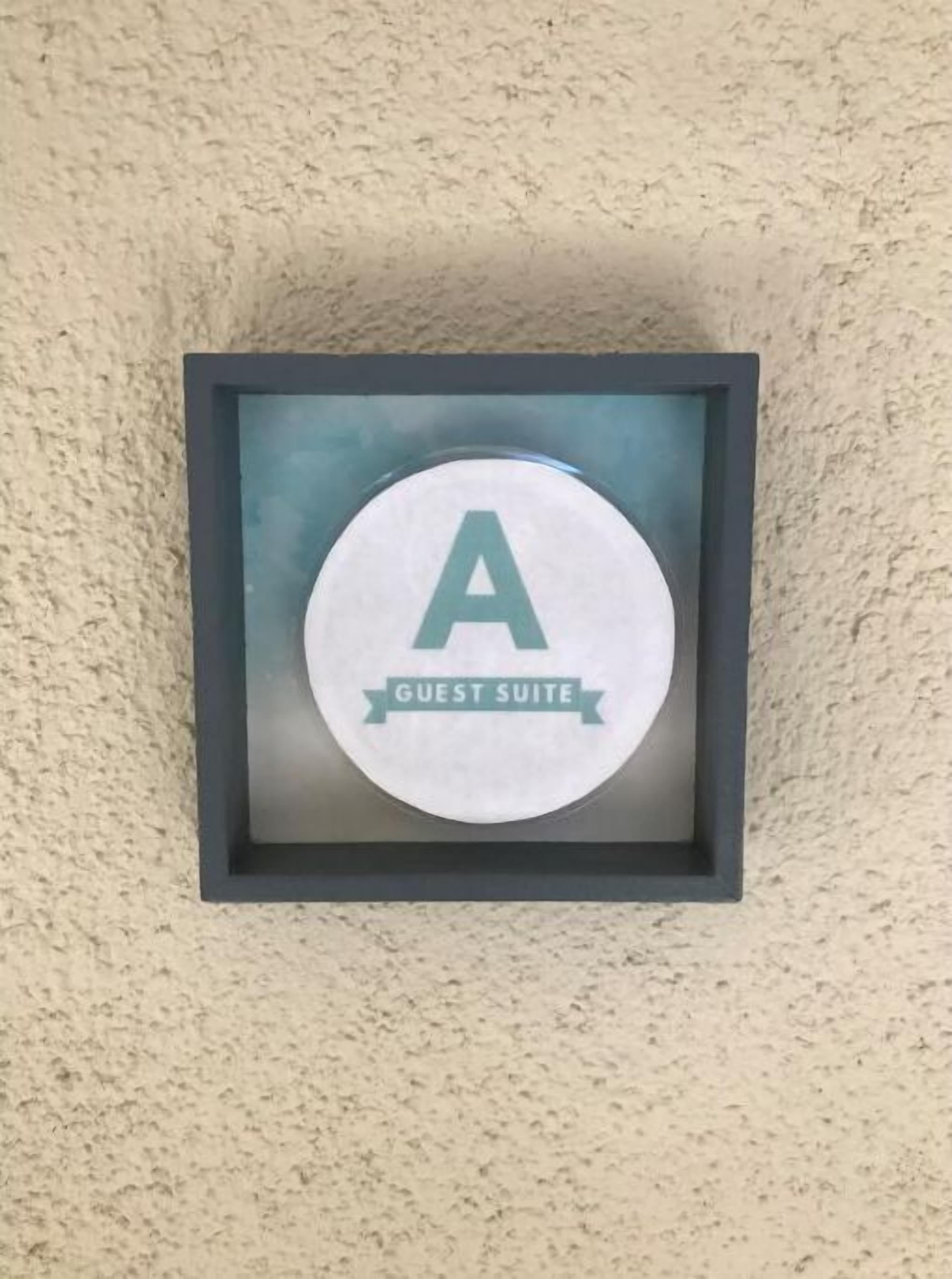 Un cartel enmarco con una 'A' grande y la leyenda 'SUITE DE HUÉSPEDES', que indica una habitación o área específica en un hotel.