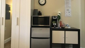 A compact kitchenette with a microwave, coffee maker, and refrigerator. A clock and a small cabinet are also visible.