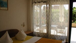 A hotel room with a bed, pillows, a bedside table, and a window with patterned curtains. - Room in Vodice with Balcony, Air condition, WIFI (4826-3) (Vodice)