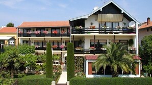 Un edificio de dos pisos con balcones, una antena parabólica y un jardín bien cuidado con diversas plantas y flores.