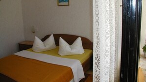 Un dormitorio con cama, almohadas, una mesita de noche, un cuadro en la pared y una cortina de encaje.