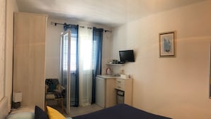 A bedroom with a bed, a desk, a chair, a television, and a window with curtains.