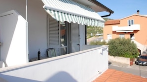 A balcony with a striped awning, a window with shutters, and a view of a street and neighboring buildings.