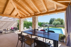 An outdoor covered patio with a pool, stone pillars, and a dining table with chairs.
