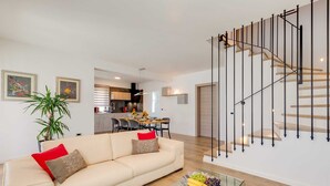 A modern living room with a sofa, a glass coffee table with fruit, a staircase with a minimalist design, and a kitchen in the background. - Villa Lyan with Swimming Pool (Tar Vabriga)