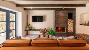 A modern living room with a stone wall, a fireplace, and a television mounted above it. - Villa Ferna with Pool (Golaš)