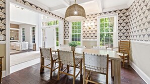 A dining area with a wooden table and chairs, a hanging light fixture, and patterned wallpaper. - Private Lakefront Escape, Launch boat from dock, swim island, hot tub, game room (Berrien Springs)