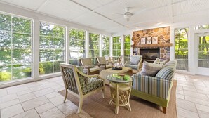 A sunroom with large windows, wicker furniture, a stone fireplace, and a herringbone floor pattern. - Private Lakefront Escape, Launch boat from dock, swim island, hot tub, game room (Berrien Springs)