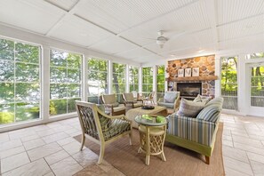 A sunroom with large windows, a stone fireplace, wicker furniture, and a herringbone floor pattern.