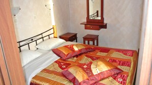 A bedroom with a bed, a nightstand, a dresser, a mirror, and a wall-mounted shelf. - Kokalakis Hotel (Kos)