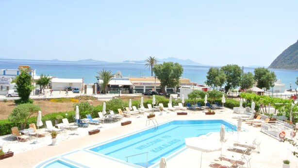 Un área de piscina con sillones de descanso y sombrillas, vista despejada al mar y montañas al fondo.