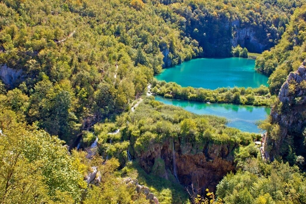 A natural landscape with a turquoise lake surrounded by dense forest and cliffs.