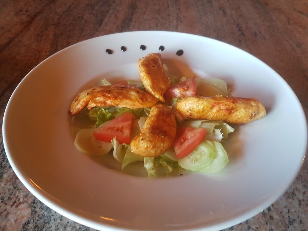 A white bowl containing a salad with grilled chicken pieces, lettuce, and tomatoes.
