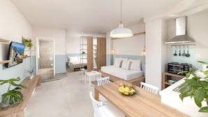 Une pièce moderne et bien éclairée, avec une table à manger en bois, des chaises blanches, un canapé et un coin cuisine équipé d’une cuisinière et de rangements suspendus pour les ustensiles.