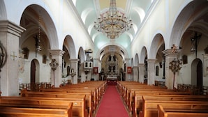 En kyrkinteriör med träbänkar, en röd matta som löper längs mittgången och en stor kristallkrona.
