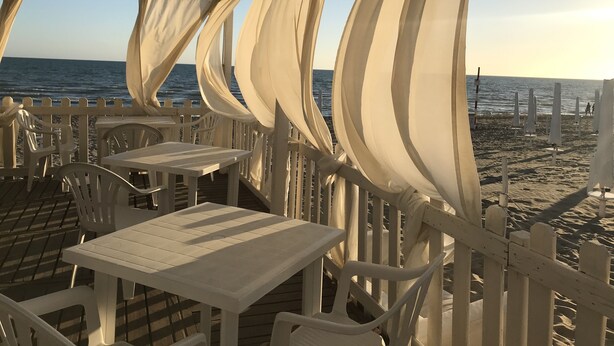 Un restaurant situé en bord de mer, avec des tables et des chaises blanches, une terrasse en bois et une vue sur l’océan.