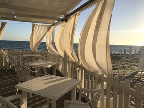 A beachside restaurant with white tables and chairs, a wooden deck, and a view of the ocean. - Designer apartment with private sea access 20 minutes from Rome (Torvaianica)