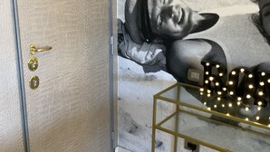 Une pièce avec une porte à la texture particulière, un sol en marbre et une fresque murale représentant une personne allongée.