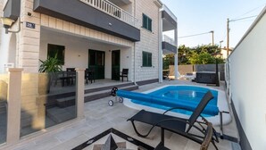 Ett modernt hus i två våningar med en swimmingpool, utomhusmöbler och en täckt uteplats.