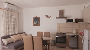 A compact living space with a sofa, dining table, chairs, kitchenette, and a window with curtains.