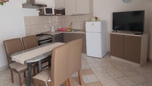 A compact kitchen with a dining area, including a stove, microwave, refrigerator, and a flat-screen TV.