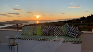 A balcony with a sofa and a chair, a bottle of champagne, and a view of the sunset over the sea. - Holiday Home in Split with Seaview, Terrace, Air condition, WIFI (4937-1) (Split)