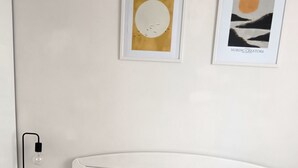 Ein Schlafzimmer mit weißem Kopfteil, zwei senfgelben Kissen, einem Nachttisch mit Lampe und zwei gerahmten Kunstwerken an der Wand.