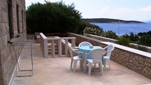 Eine Terrasse im Freien mit Tisch und Stühlen, Steinmauern und Meerblick.