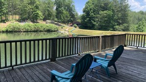 A wooden deck with two chairs and a table overlooking a lake, surrounded by trees and a grassy area. - Lakeside Retreat: Explore 35 acres of wilderness and private lake, hot tub (Ellijay)