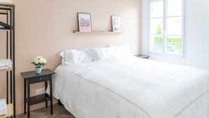 Un dormitorio con una cama grande, una mesita de noche con una planta, una estantería con fotografías y una ventana que da a zonas verdes.