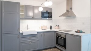 Una cocina moderna con gabinetes grises, un lavamanos blanco, una campana extractora de acero inoxidable y un suelo de madera en patrón de espiga.