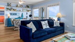 Ein Wohnzimmer mit einem blauen Sofa, einem Couchtisch und Meerblick durch große Fenster.
