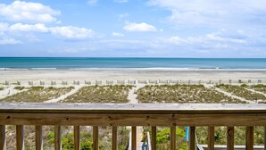 Blick auf einen Strand von einer Holzterrasse aus, mit einem Sandweg, der zum Meer führt.
