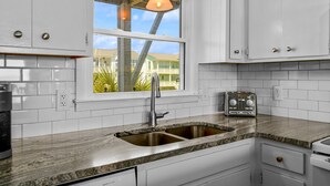 Eine Küche mit weißen Schränken, einer Granit Arbeitsplatte, einer Spüle, einem Toaster und einem Fenster mit Blick auf Häuser.