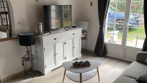 A modern living room with a sofa, a wicker chair, a coffee table, a TV on a cabinet, and a view of the outside. - Family vacation home with beach and spa (Barbâtre)
