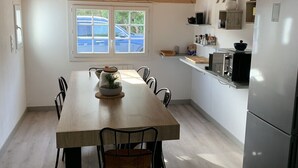 A modern kitchen with a wooden dining table, chairs, a refrigerator, and a window with a view of parked cars outside. - Family vacation home with beach and spa (Barbâtre)